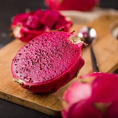 Close-up of a halved Red Dragon Fruit (Pitaya) on a wooden cutting board, revealing the magenta-red flesh and tiny black seeds